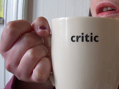 A hand holds a cream colored cup with the word critic on the side