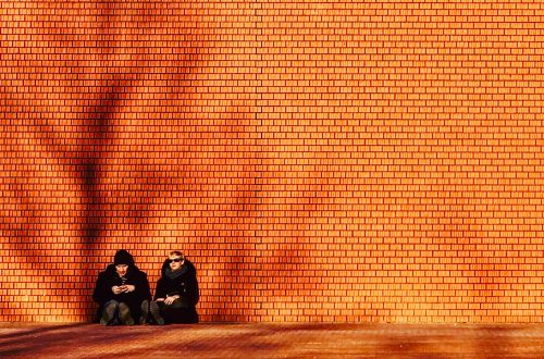 man and woman in black coat sitting against brown wall