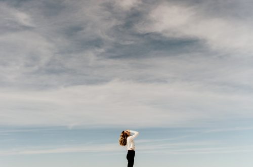 woman looking up to the sky while standing on white sand