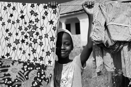 grayscale photo of boy in hat holding clothes hanger rope with clothes